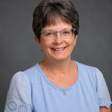 Middle-aged woman with short hair and glasses smiling against a gray background.