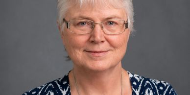 Portrait of a smiling elderly woman with glasses against a plain background.