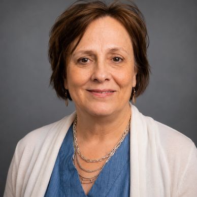 Portrait of a middle-aged woman smiling gently against a grey background.
