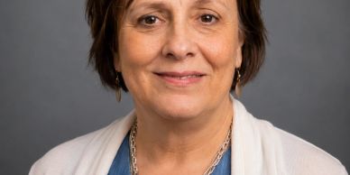 Portrait of a middle-aged woman smiling gently against a grey background.