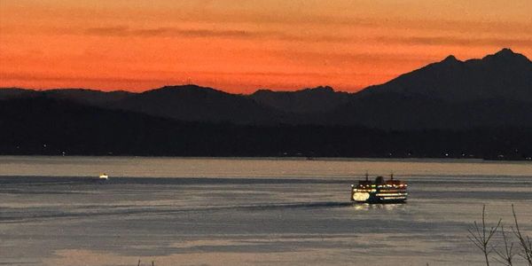Boat sailing on calm water during sunset with mountains in the background.