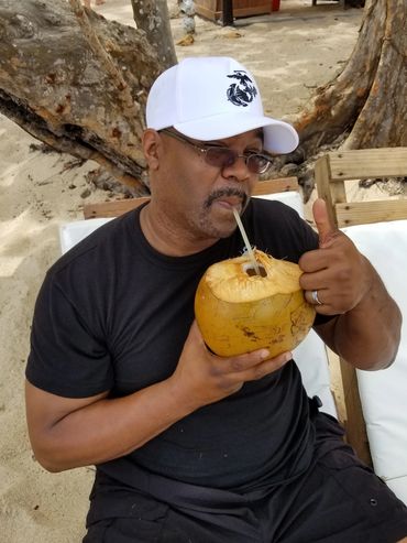 Man in white cap drinking from a coconut and giving thumbs up.