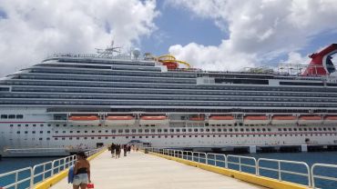 Large cruise ship docked at the port with passengers walking on the pier.