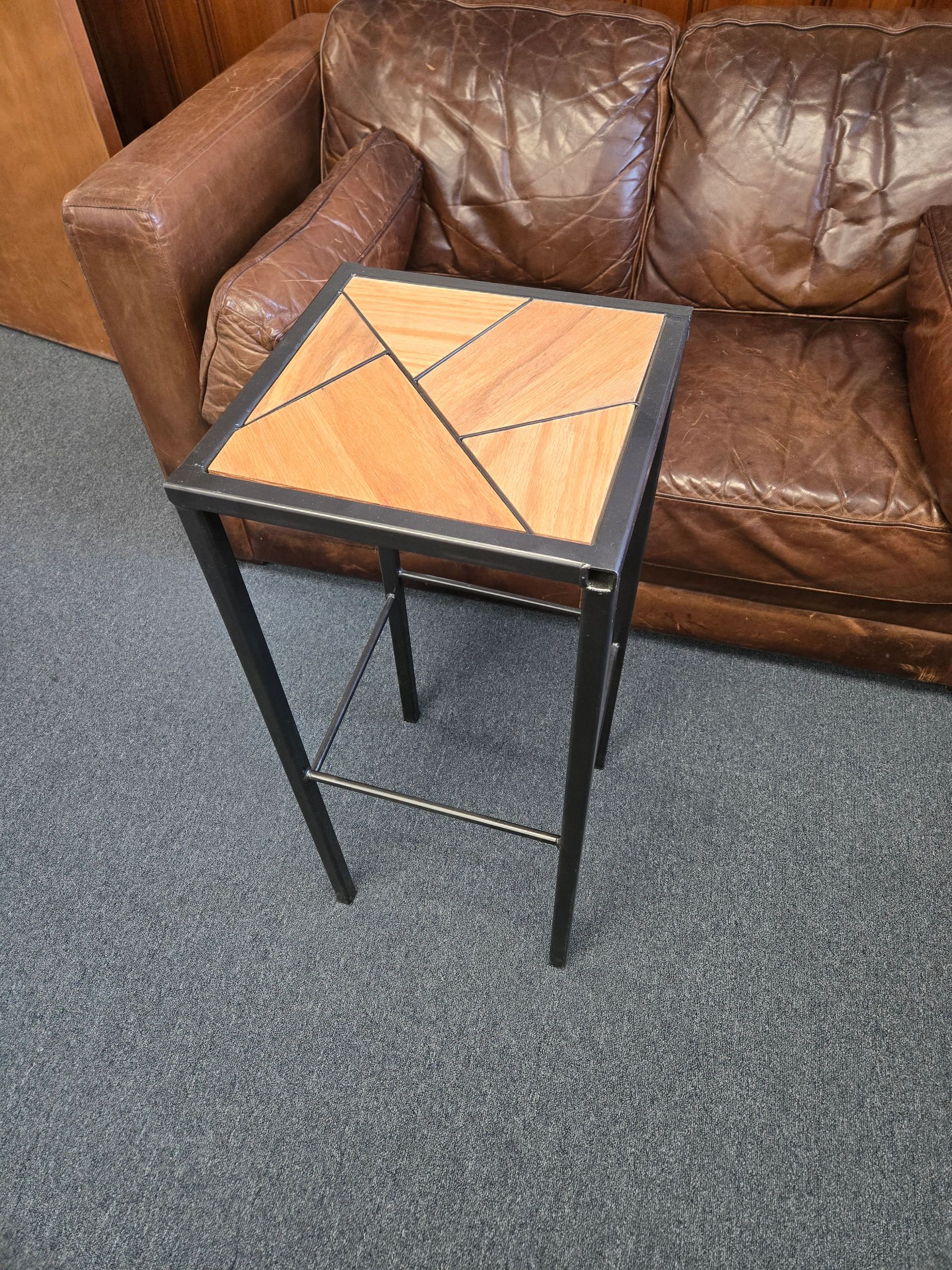 Tall wooden side table with geometric design beside a brown leather sofa.