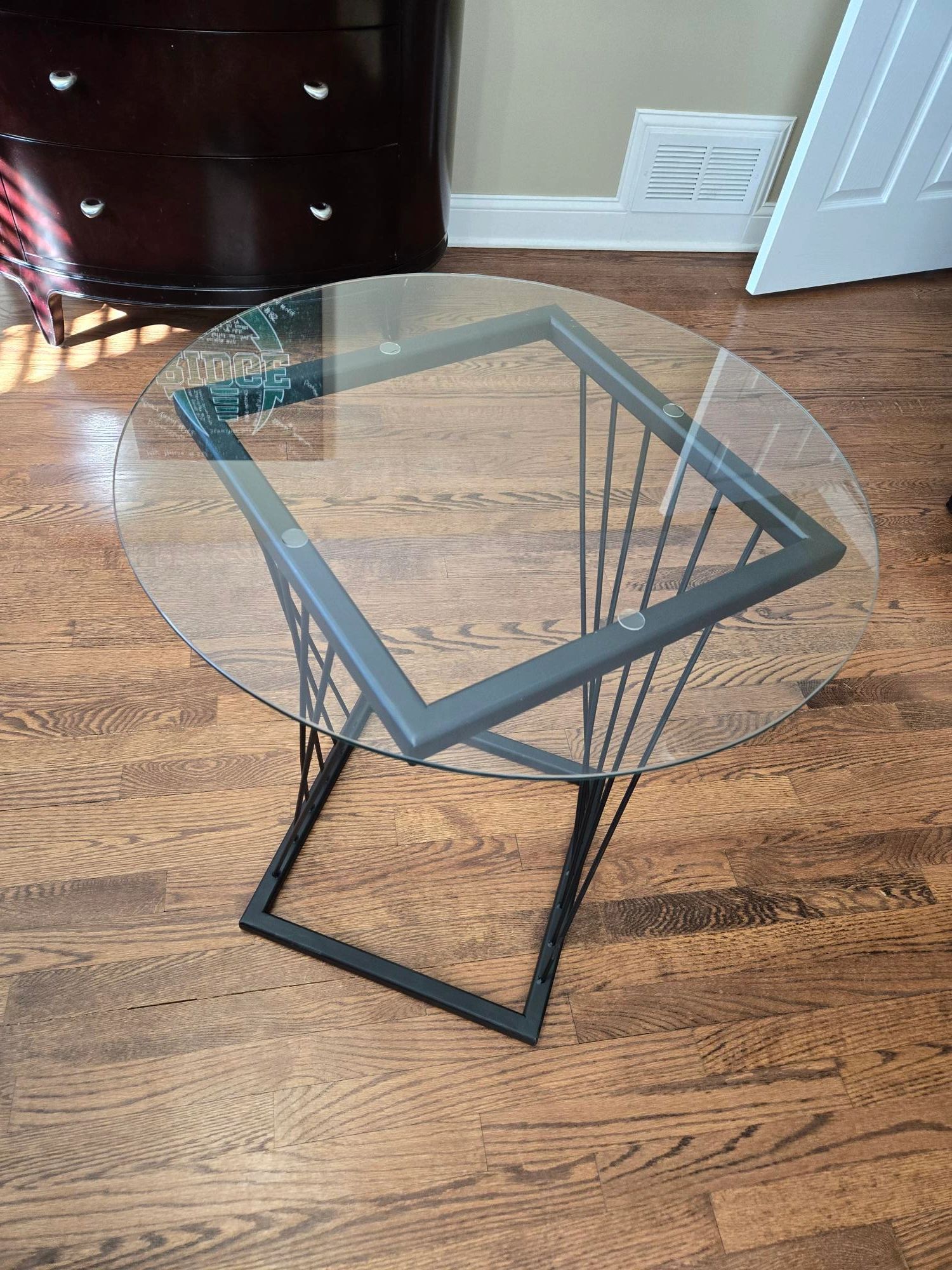 Modern round glass table with a geometric metal base on wooden floor.