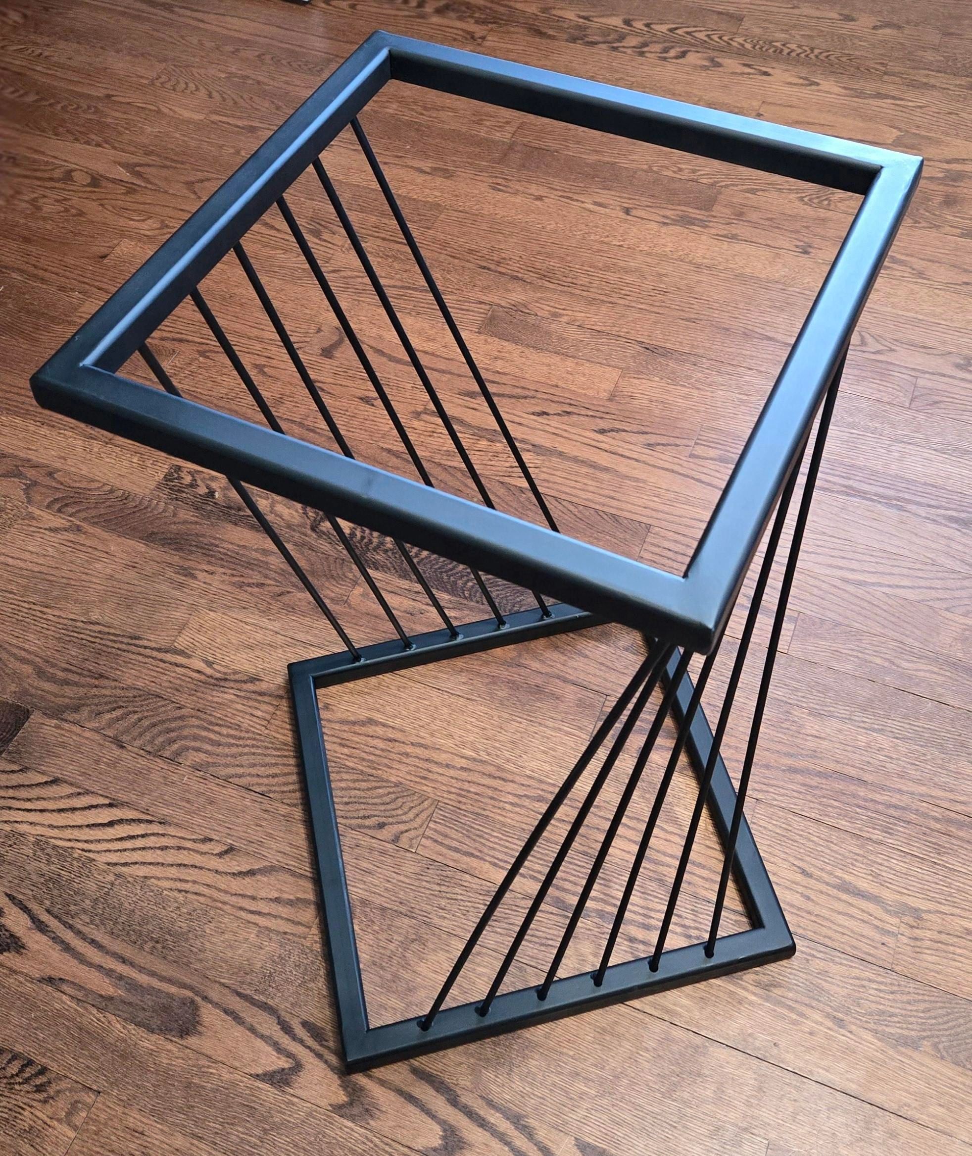 Modern black metal side table with geometric design on wooden floor.