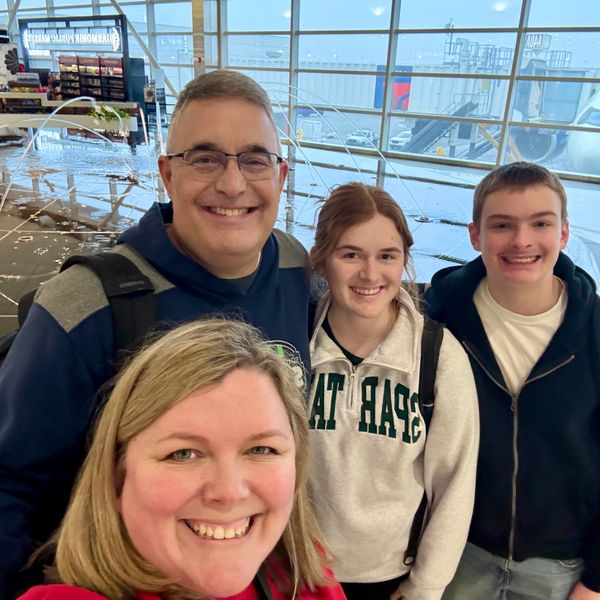 A happy family of four smiling at the airport terminal.