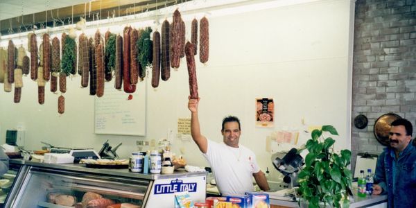Man holding up a large sausage in a deli shop.