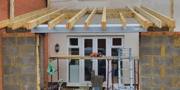 Construction site showing a partially built wooden roof over a brick structure.