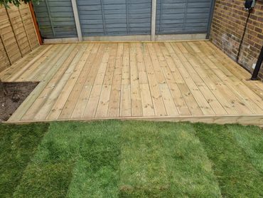 Newly installed wooden deck adjacent to fresh green grass in a backyard.
