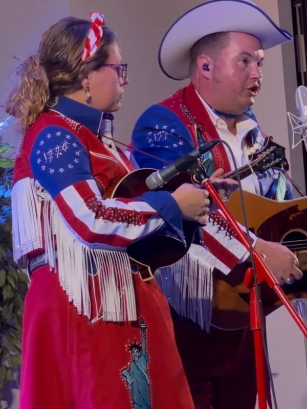Two musicians in patriotic outfits playing guitar and mandolin on stage.