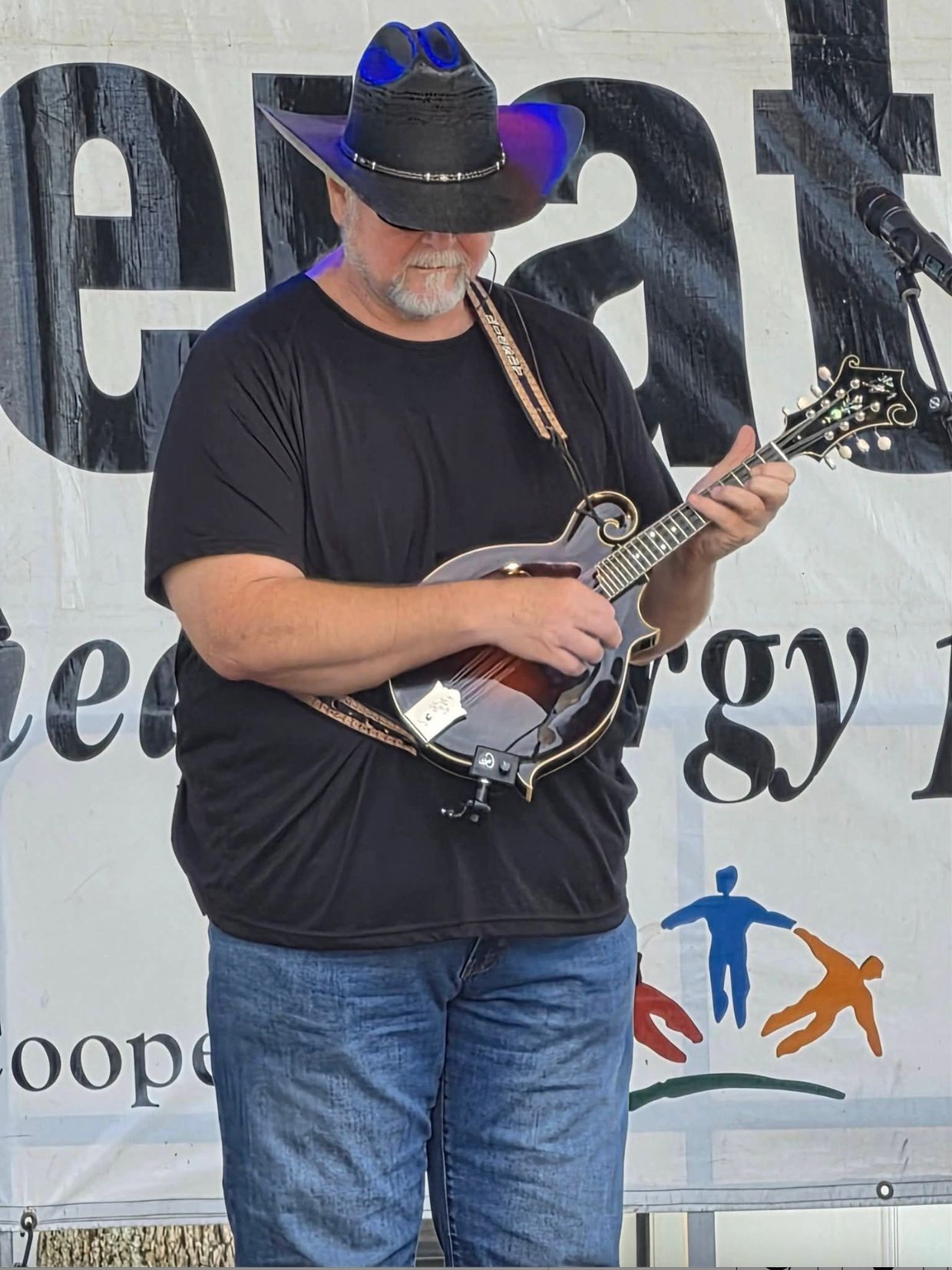 Man in black shirt and cowboy hat playing mandolin on stage.