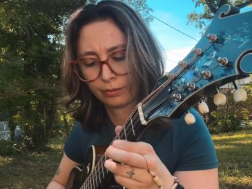 Woman playing a mandolin outdoors in a serene garden.