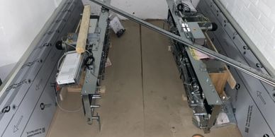 Two metal machine parts on a floor in a room under construction.