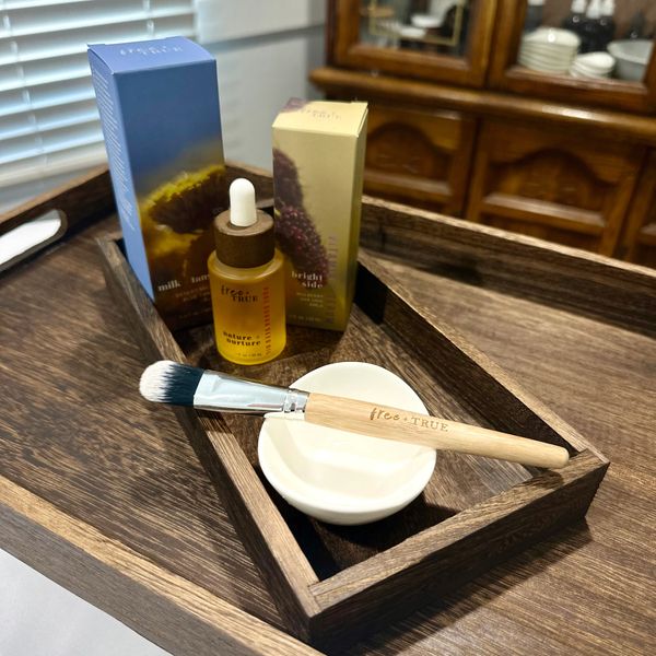 Skincare products and a brush on a wooden tray with a small white bowl.