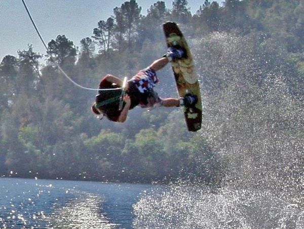 Person wakeboarding mid-air over a lake with water splashing.