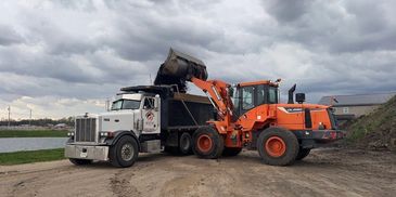 An orange loader dumping gravel into a white dump truck on a cloudy day.