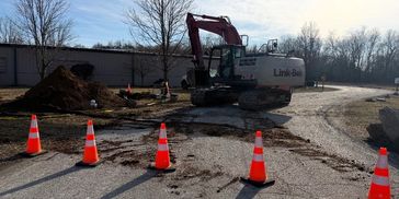 Construction site with an excavator and traffic cones blocking the road.