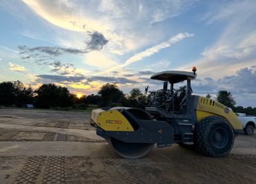 A yellow road roller parked on a construction site during sunset.