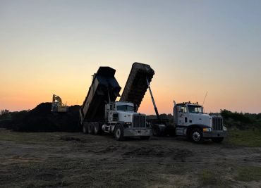 Dump trucks unloading soil at sunset.