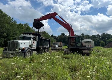 Excavator loading soil into a dump truck in a field.