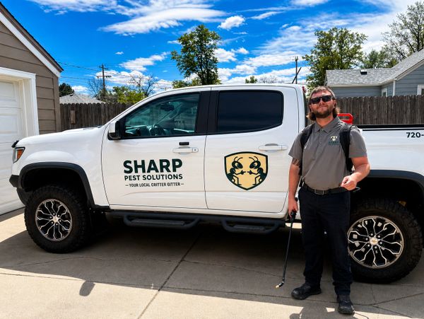 Man standing next to a Sharp Pest Solutions truck under a blue sky.