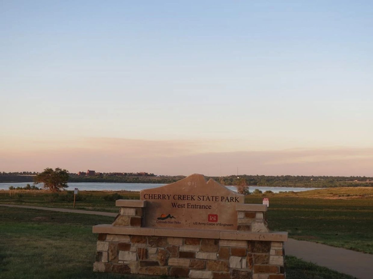 Entrance sign to Cherry Creek State Park with a lake in the background at sunset.