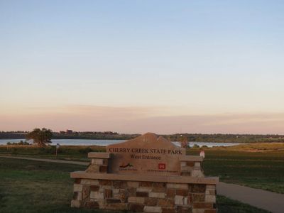 Entrance sign to Cherry Creek State Park with a lake in the background at sunset.