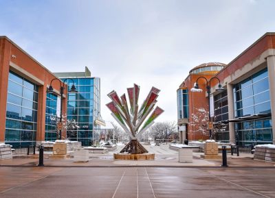 Modern sculpture in a plaza between two buildings on a cloudy day.