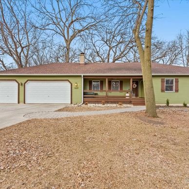 Single-story green house with a large driveway and bare trees in the yard.