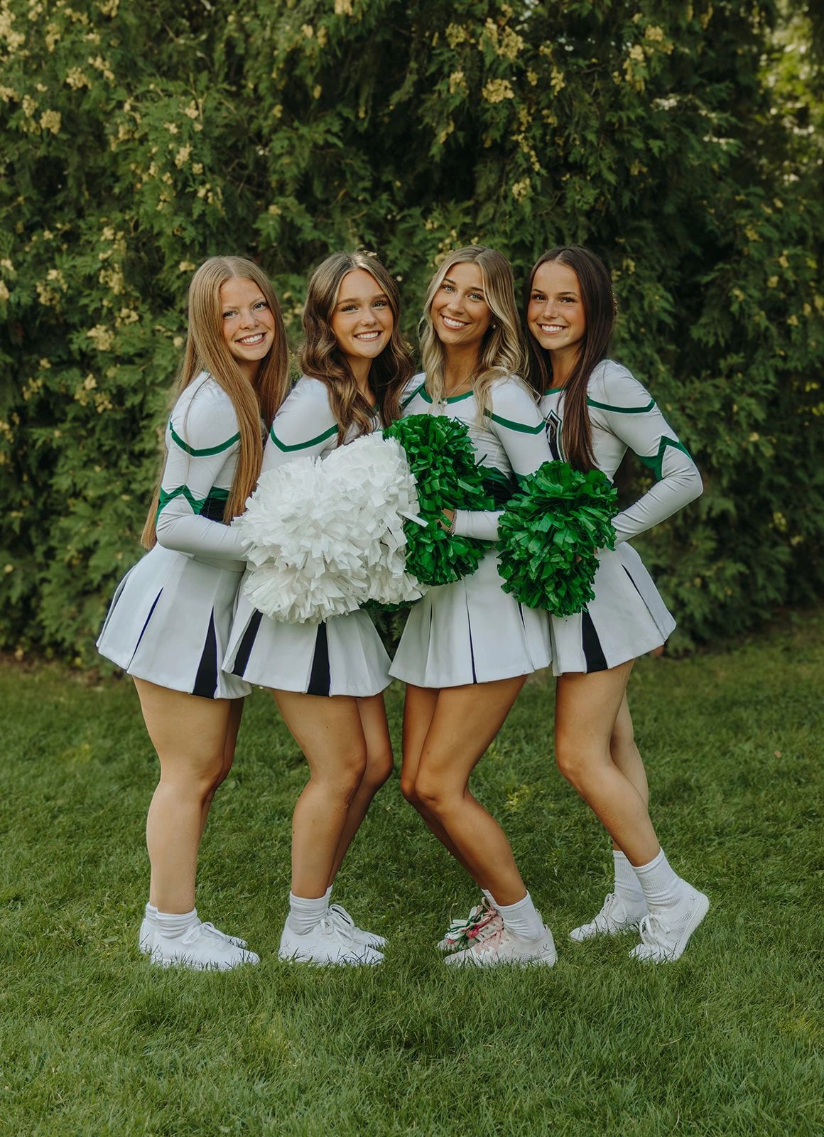 Four cheerleaders posing with pom-poms on grass.