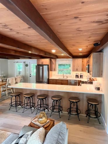 Rustic kitchen with wooden ceiling and stools at the counter.