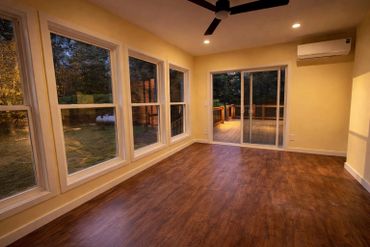 Empty room with wooden floor and large windows showing outdoor greenery.