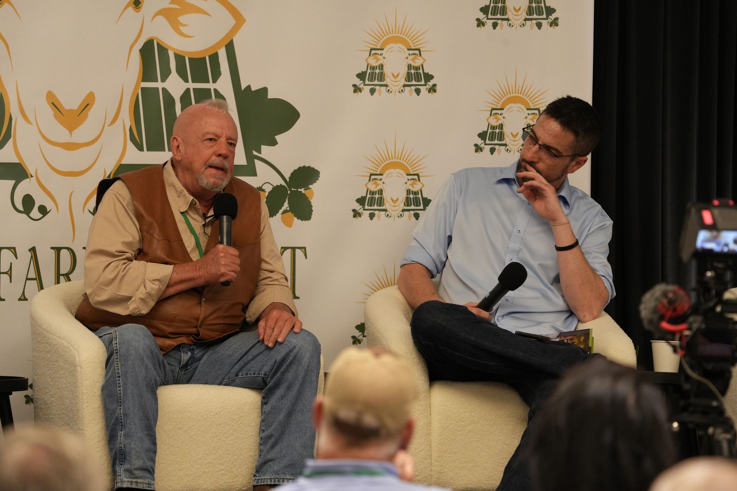 Two men having a discussion on stage, one speaking into a microphone.