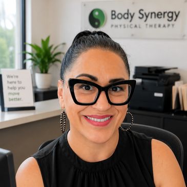 Smiling woman with large glasses in a physical therapy office.