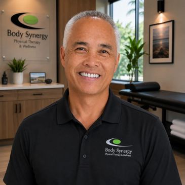 Smiling man in a Body Synergy polo shirt inside a therapy room.