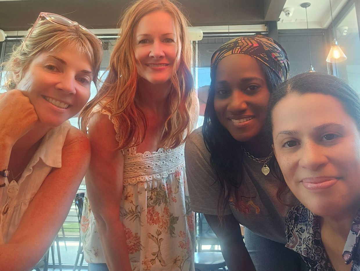 Four women smiling inside a café.