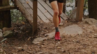 Runner's legs with red shoes on a forest trail near a wooden bridge.