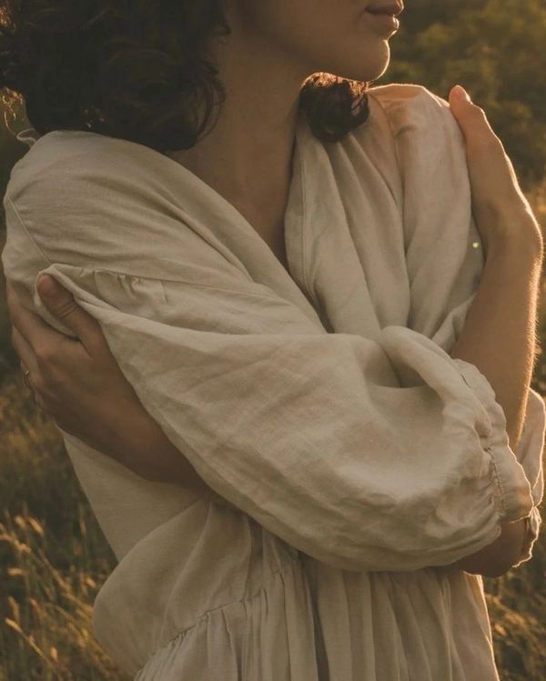 Woman hugging herself in a soft beige dress during golden hour.