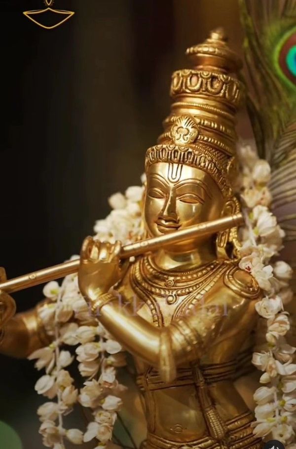 Golden statue of Lord Krishna playing the flute adorned with garlands.