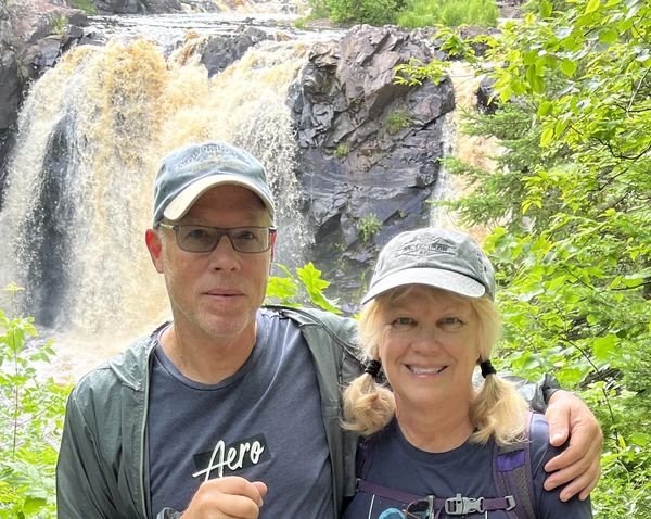 Couple smiling with waterfall and greenery in the background.
