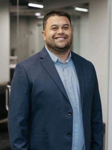 Smiling man in a blue suit jacket standing indoors.