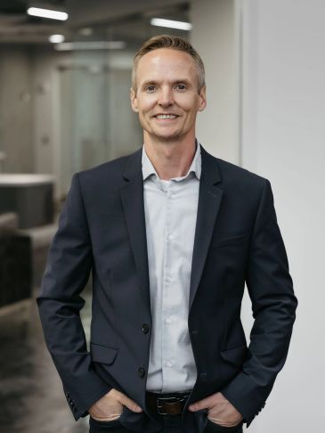 Smiling man in a dark suit in an office setting.