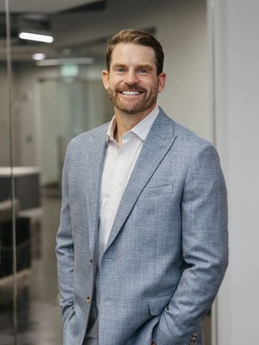 Man smiling in a gray suit jacket in an office.