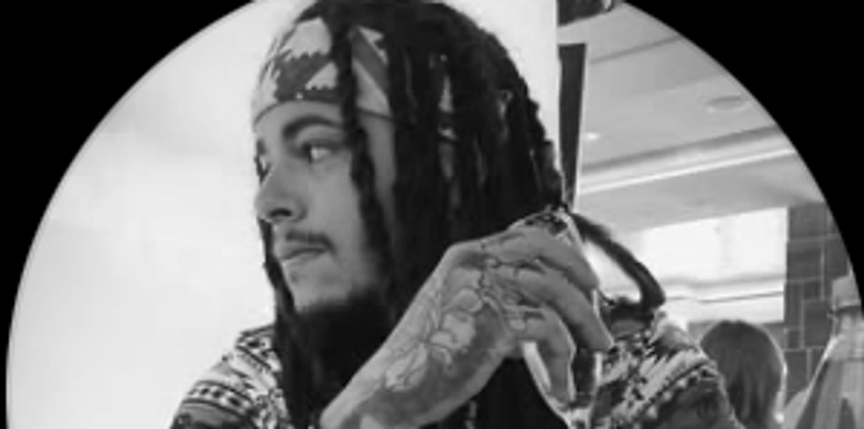 Man with dreadlocks and tattoos, looking contemplatively to the side.