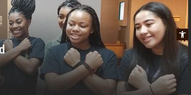 A group of young women smiling and crossing their arms in a friendly gesture.
