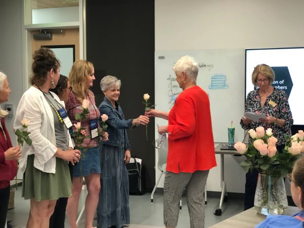 Women exchanging roses during a meeting or ceremony indoors.