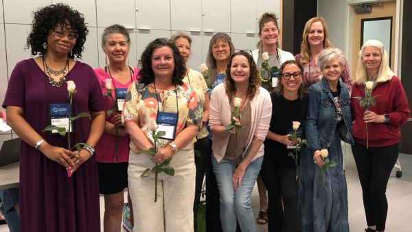 Group of women holding white roses in a classroom setting.