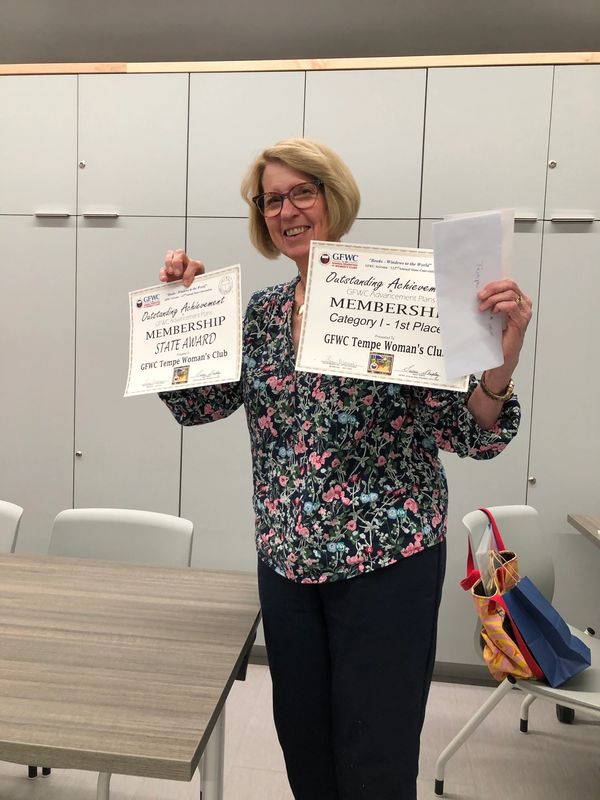 Woman proudly holding membership achievement awards from GFWC Tempe Woman's Club.