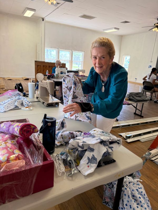 Elderly woman arranging colorful fabric pieces on a table in a sewing room.